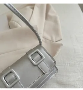 Close-up of metallic silver leather shoulder bag showing square buckle and fine stitching