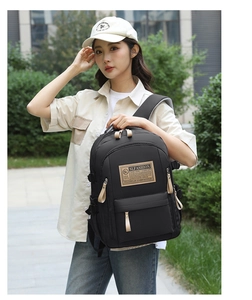 Detail of black nylon backpack featuring brown leather logo patch and adjustable side straps