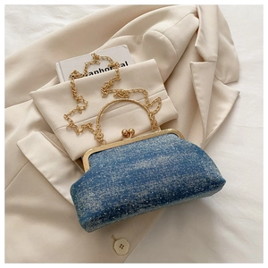 Detail view of blue denim shell bag with gold handle on beige blazer and white book