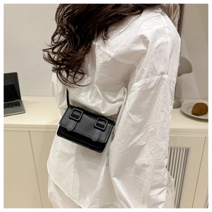 Detail of a minimalist black mini flap bag with double buckles worn as a crossbody purse