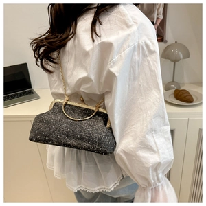 Detail of black tweed crossbody bag with gold frame and chain strap in a lifestyle setting