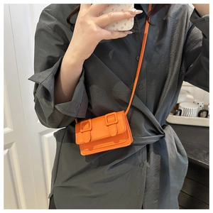 Detail of bright orange mini crossbody bag with double buckle design on a female model