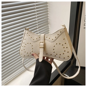 Gros plan sur un sac en cuir gaufré blanc cassé avec des clous dorés et boucle en métal