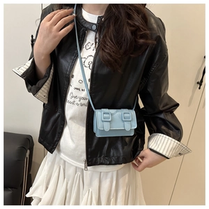Close-up of light blue mini messenger bag with double buckles worn over a leather jacket
