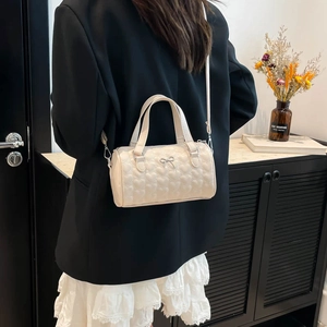Creamy white quilted Boston bag with heart patterns and silver bow worn as a crossbody