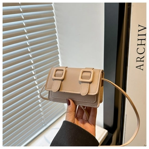 Close-up of a beige faux leather crossbody bag with buckle detail in natural light