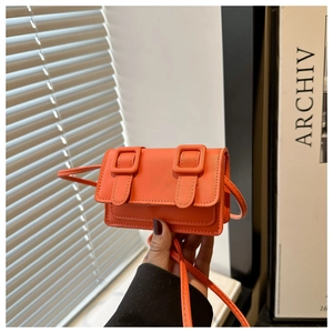 Detail of orange mini crossbody bag with double-buckle flap and faux leather texture