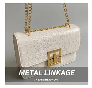 Close-up of crocodile embossed texture on white bag with gold chain and metal lock