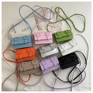 Flat lay of colorful mini crossbody bags with dual square buckle decor on white fabric