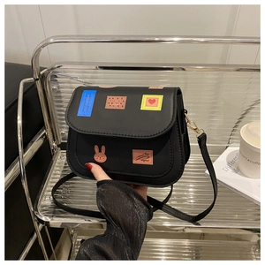 Detail of black crossbody bag with colorful patches on a metal shelf with props