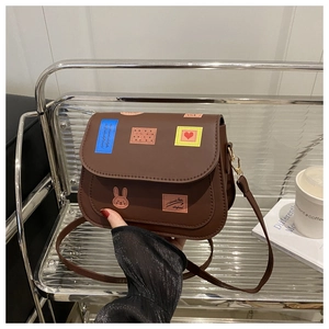Detailed view of brown PU crossbody bag featuring colorful rabbit patches and badges
