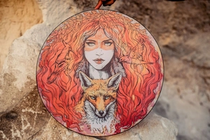 Detail of creative decorative drum featuring woman and wolf art in a natural setting