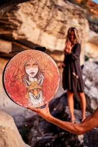 Artistic shaman drum with red fox and woman illustration displayed in nature