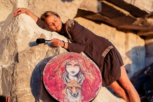 Macro detail of shaman hand drum featuring woman and fox art with mallet on rocky cliff