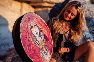 Outdoor shot of a shamanic drum with red-haired woman and fox art in golden sunset light