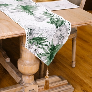 Ink wash palm leaf table runner with golden tassels on a rustic wooden dining table