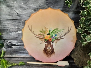 Detail of colorful deer head painting on shaman frame drum with wooden mallet and ivy