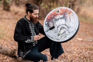 Artistic shaman drum featuring tree of life and wolf illustration in a forest setting