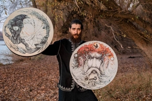 Detail of Shaman drums with Tree of Life and raven art held by a person in a forest