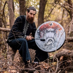 Shaman drum with Tree of Life and wolf patterns being played in a forest setting