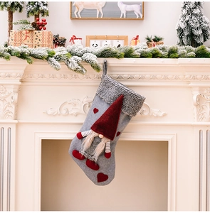 Detail of grey knitted Christmas stocking with gnome and red heart on a white fireplace