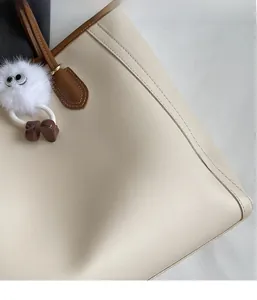 Detail of off-white tote bag showing brown leather handles and plush monster charm