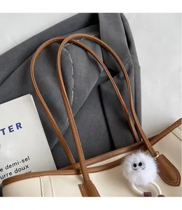 Detail of a beige PU leather tote bag with brown handles and a white plush charm
