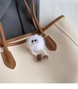 Close-up of white plush monster keychain with big eyes attached to a tote bag