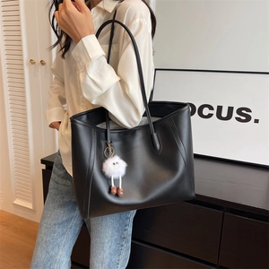 Chic black PU leather tote bag with a white plush charm worn by a model in a modern room