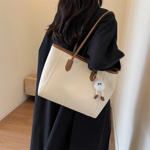 Woman in black robe carrying a large cream PU leather tote bag with a plush charm detail