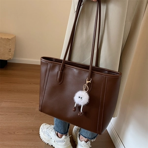 Detail of dark brown leather tote bag with plush charm on a beige trench coat