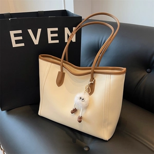 Detail of a large cream tote bag with brown straps and a white fur charm on a leather sofa