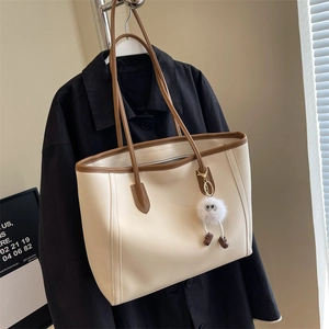Detail of cream tote bag with brown trim and cute plush charm on black blazer background