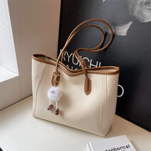 Detail view of large cream tote bag with brown handles and a cute fuzzy charm