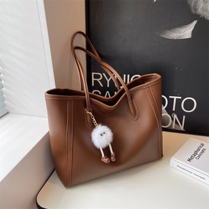 Detail of a brown PU leather tote bag with a white plush monster charm and fine texture