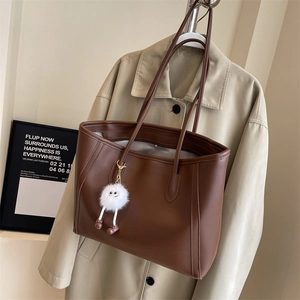 Detail of a brown PU leather tote bag with a white plush charm on a long shoulder strap