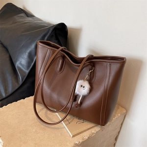 Detail of dark brown leather tote bag with plush monster charm on stone surface