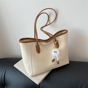 Minimalist cream faux leather tote bag with brown trim and a plush monster charm detail