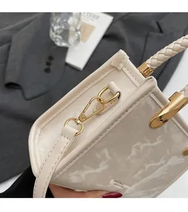 Detailed view of cream square handbag with marble texture and woven handle with gold hardware