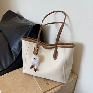 Detail view of cream and brown tote bag with premium leather texture and plush charm accessory