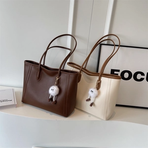 Detail of minimalist PU leather tote bags in dark brown and beige with plush charms