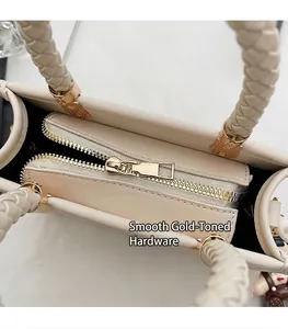 Close-up of cream square handbag showing woven handle and smooth gold metal zipper detail