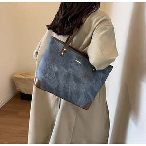 Detail of vintage tote bag with blue washed texture, brown leather trim, and metal accents