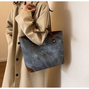 Detail of blue textured tote bag with brown leather trim and golden metal rivet hardware