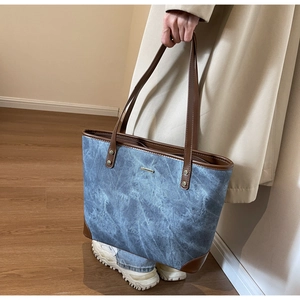 Detail of blue denim tote bag with brown leather trim and metallic rivets in a cozy setting