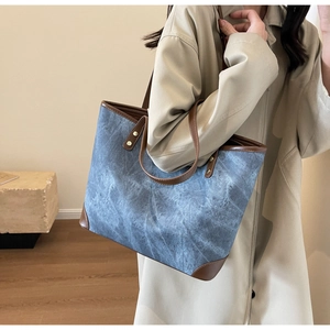 Detail of blue denim tote bag with brown leather trim and gold rivet accents on side