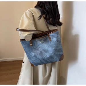 Detail of blue textured tote bag with brown leather trim held by woman in trench coat