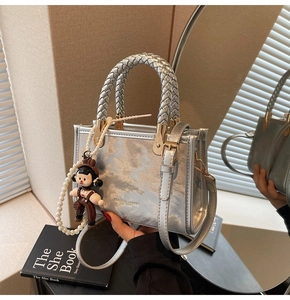 Detail of silver textured handbag with woven handle, pearl bead strap and charm