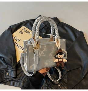 Close-up of silver crossbody bag with marble texture and cute doll charm on black leather