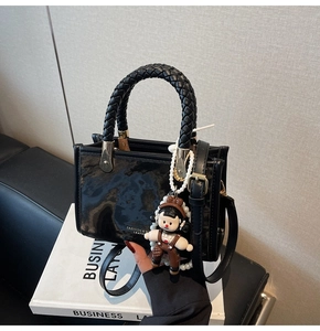 Detail of black mini handbag featuring woven top handle, marble texture, and pearl charm
